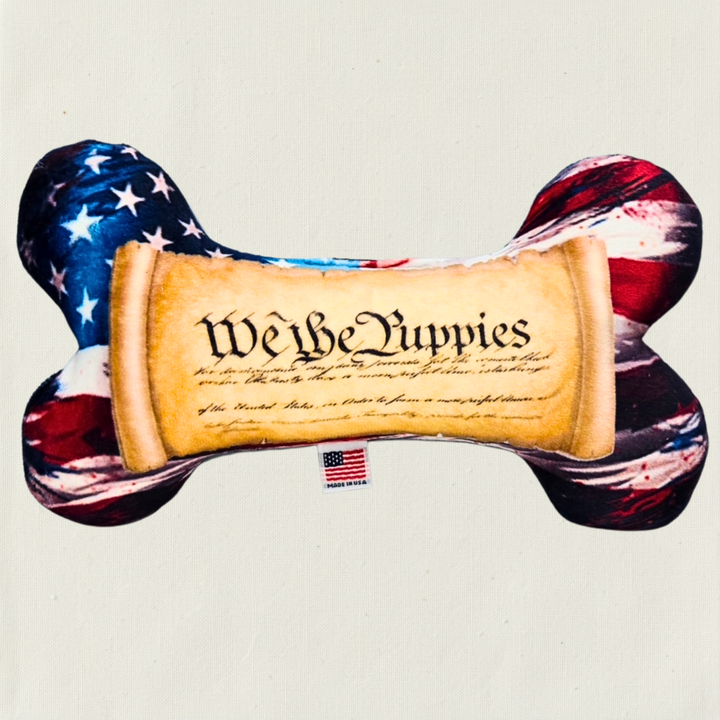 Dog toy shaped like a bone with American flag and 'We the Puppies' text on a light tan background that looks like the constitution. 